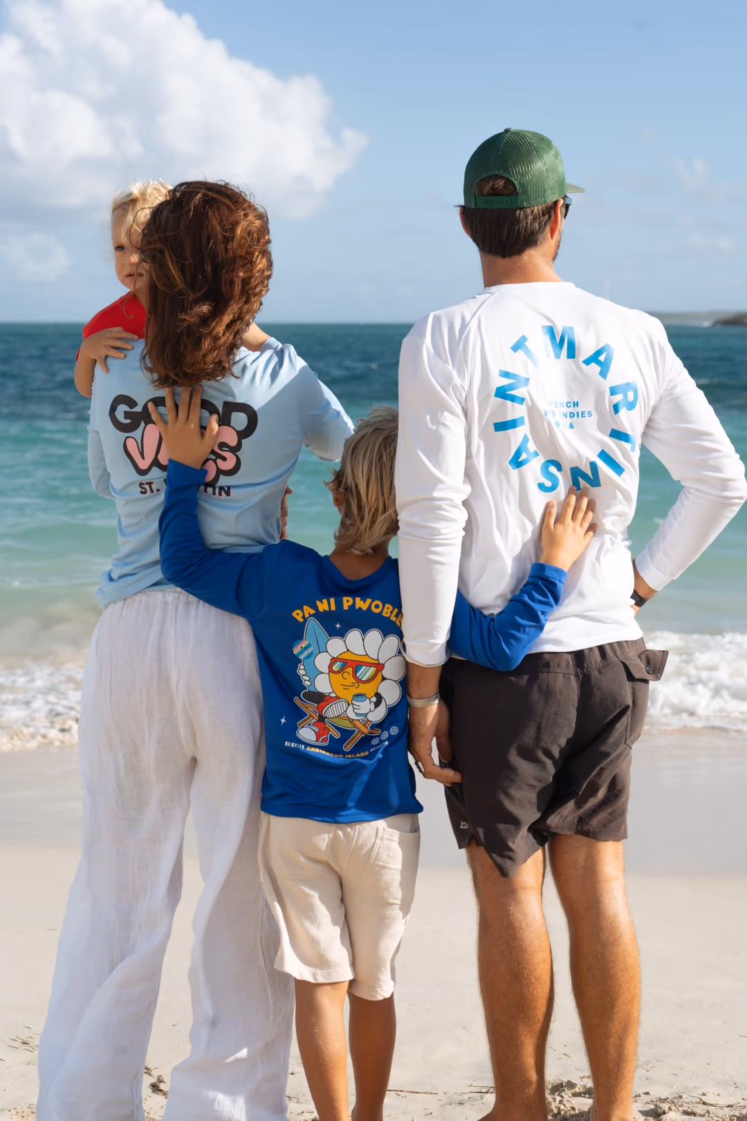Une famille marche sur une plage de Saint-Martin, portant des t-shirts illustrés OLDA.